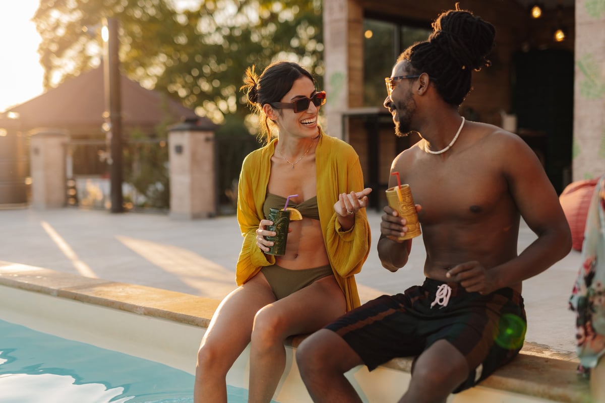 Young couple relaxing by the pool with tropical cocktails, enjoying the sunset