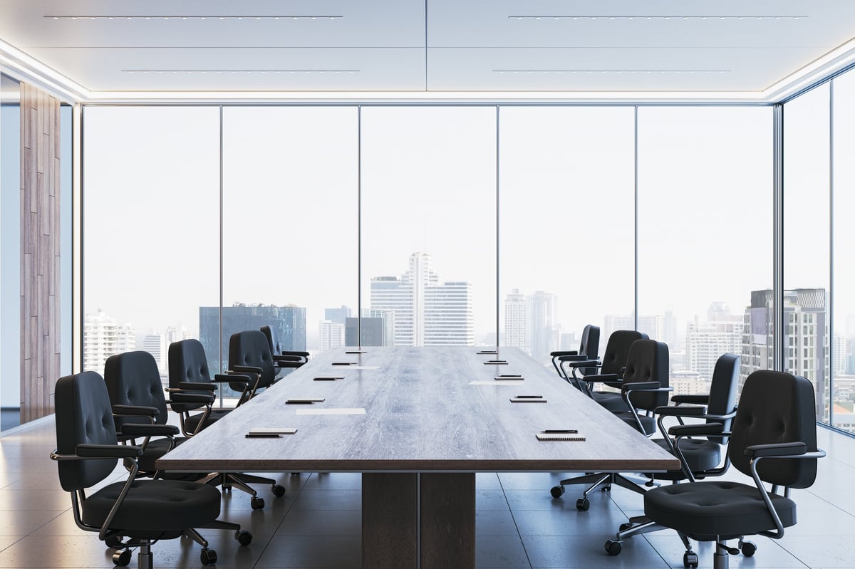Spacious corporate boardroom with sleek black chairs, a long wooden desk, and floor-to-ceiling windows offering a city view