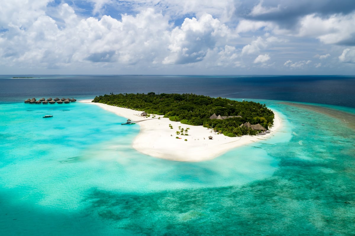 Aerial view of Maldives atoll resort shows overwater villas