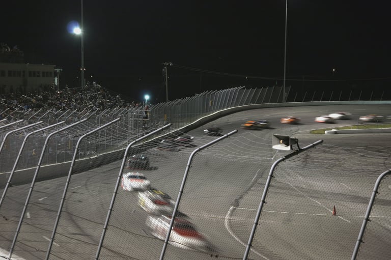 Night racing event with multiple race cars on an oval track